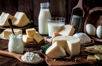 Various types of cheese, milk, and dairy products arranged on a wooden table with a rustic background.