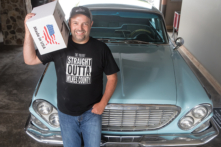  Brian Call holds a case of moonshine in front of his father’s 1961 Chrysler New Yorker Golden Lion edition, which used to haul moonshine to Charlotte and Winston-Salem.