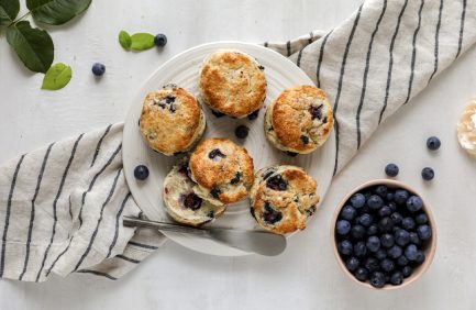 A plate of freshly baked blueberry scones on a white surface, surrounded by blueberries and a striped napkin.