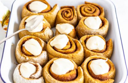 Freshly baked cinnamon rolls topped with dollops of creamy white icing, arranged closely together in a baking dish.