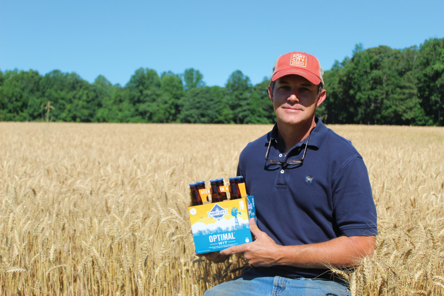 Rob Hinton holds a 6-pack of Optimal Wit craft beer in one of his fields