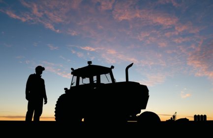 Silhouette of a farmer and a tractor at sunrise