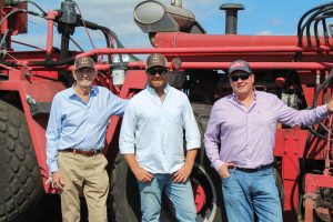 Cooper Hopkins with his grandfather and dad pose for a photo in front of farming equipment