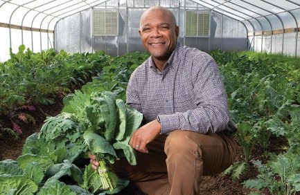 Marlon Foster holds Collard Greens and Kale inside one of the green houses at Green Leaf Learning Farm.