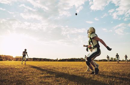 athletes who farm; American football players running to catch a pass during team practice drills on a football field in the afternoon