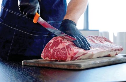 Chef cuts raw meat on the wood board with the knife, close-up. Chopping meat for cooking steak at reastaurant.