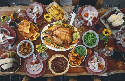 A festive dinner table set with roast turkey, corn on the cob, green beans, sweet potatoes, pie, bread, and various side dishes.
