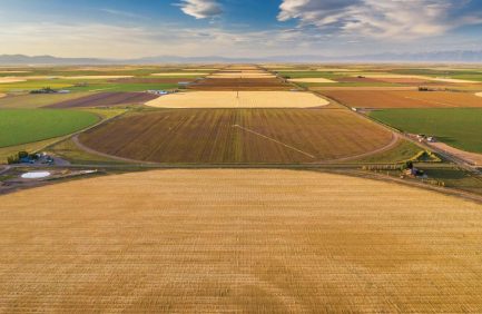 Aerial view of large, colorful farmland plots under a blue sky with scattered clouds.