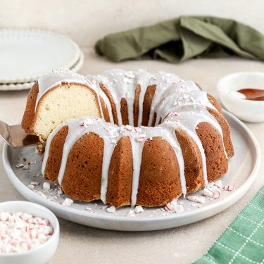 Bundt cake with white icing drizzled on top, sliced on a plate, with bowls and plates in the background.