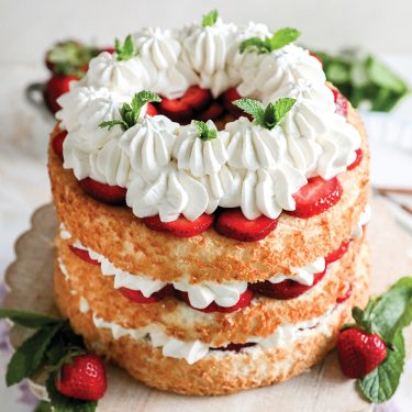 Layered strawberry shortcake with whipped cream and fresh strawberries, garnished with mint leaves, displayed on a wooden board.