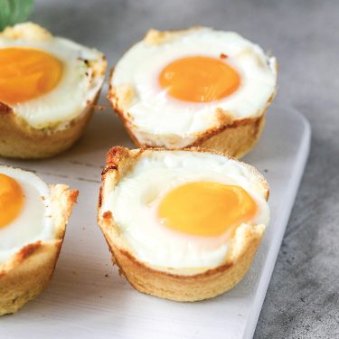 Four baked egg muffins with golden yolks on a white serving board, placed on a gray surface.
