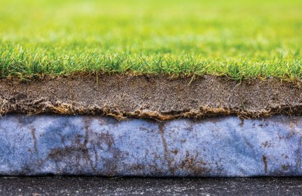 A close-up cross-section of green grass, soil layers, and underlying rock, illustrating the different layers beneath a lawn.