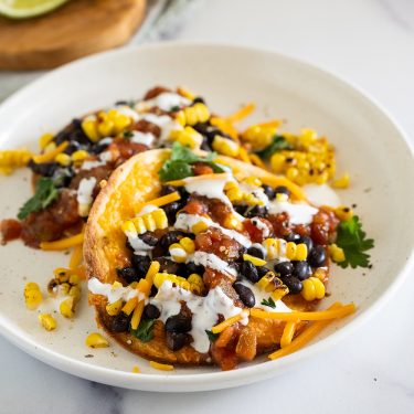 Two tacos filled with black beans, corn, cheese, cilantro, salsa, and drizzled with a white sauce, served on a white plate.