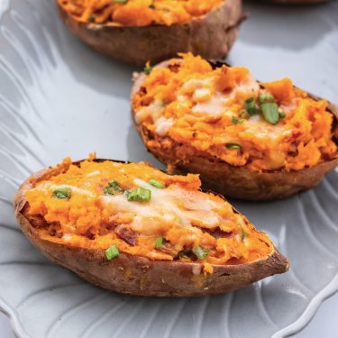 Baked sweet potato halves stuffed with mashed sweet potato, melted cheese, and chopped green onions on a light-colored plate.